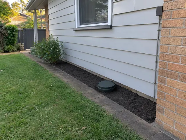Tidy soil strip with a capped sewer access beside a weatherboard house and brick wall in Mount Colah